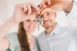 Smiling new homeowners holding up house keys with a small house-shaped keychain