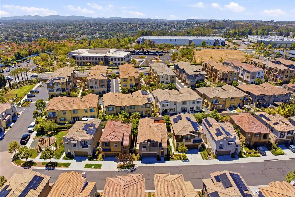 Aerial view of a North County San Diego neighborhood with tile-roof homes, solar panels, and rolling hills in the distance