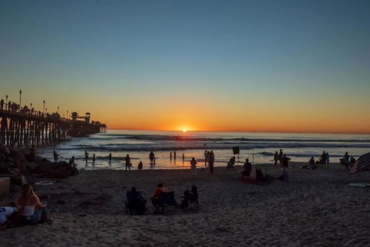 Sunset over the Oceanside Pier and beach in Oceanside, CA, with people enjoying the sand and surf