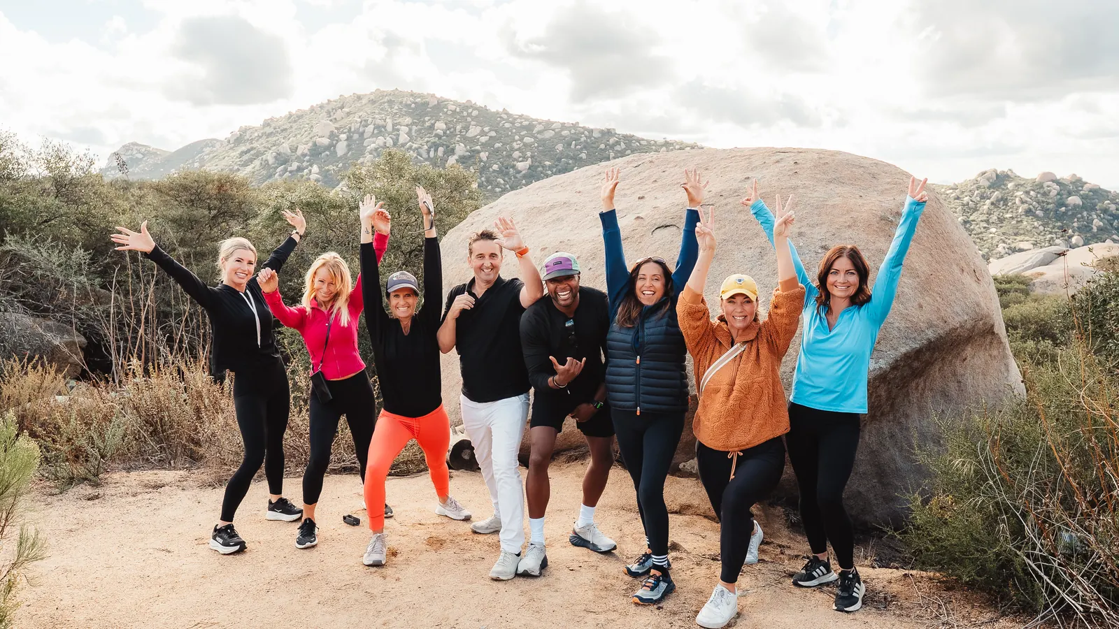 Karen Pietsch, Ty Hines, and a hiking group cheering beside a granite boulder on the Mount Woodson Trail in Poway