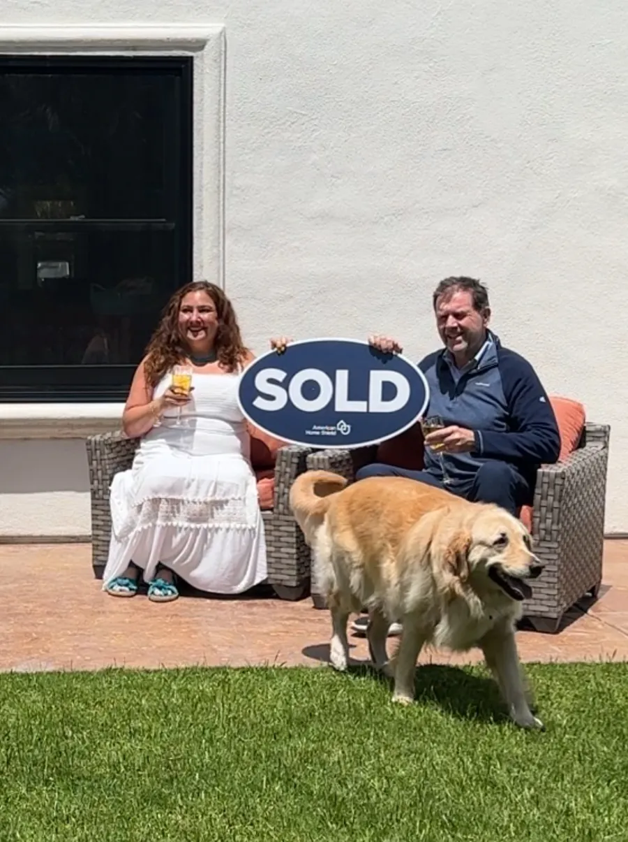 Happy homeowners holding a SOLD sign with their golden retriever