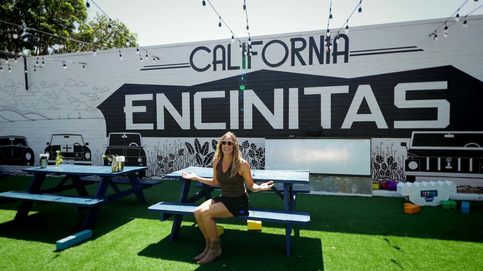 Karen Pietsch sitting at a picnic table in front of the California Encinitas mural.