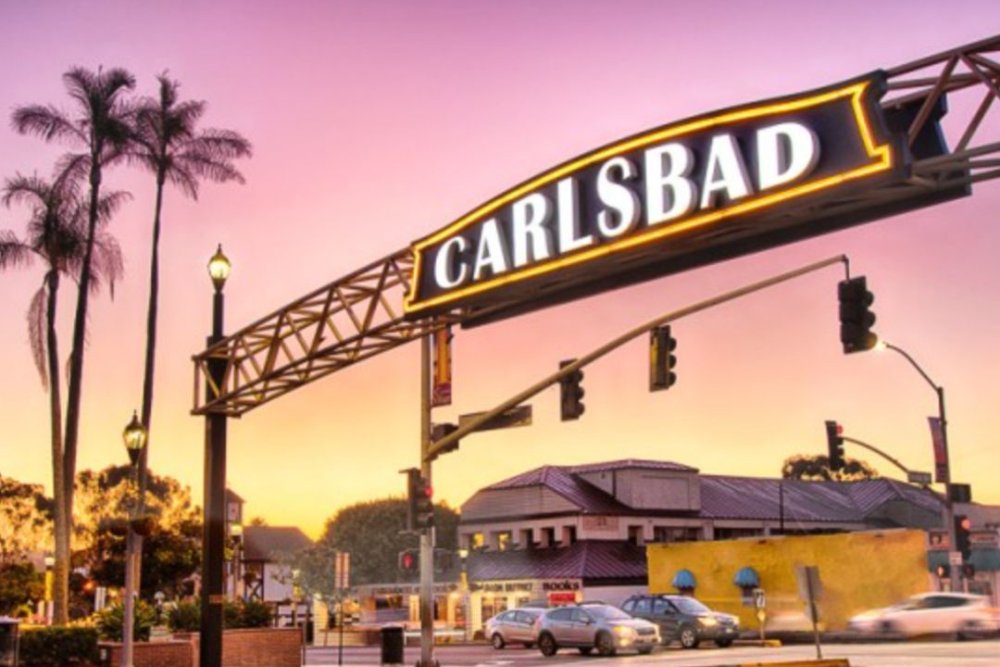 Carlsbad Village sign over Carlsbad Boulevard at sunset with palm trees