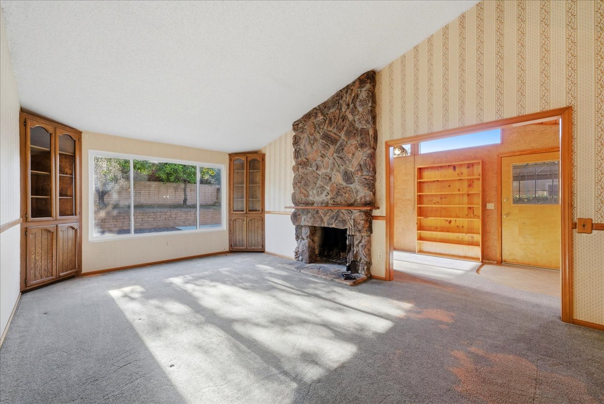 Living room with a stone fireplace, built-in wood cabinets and original wallpaper in an older North County San Diego home