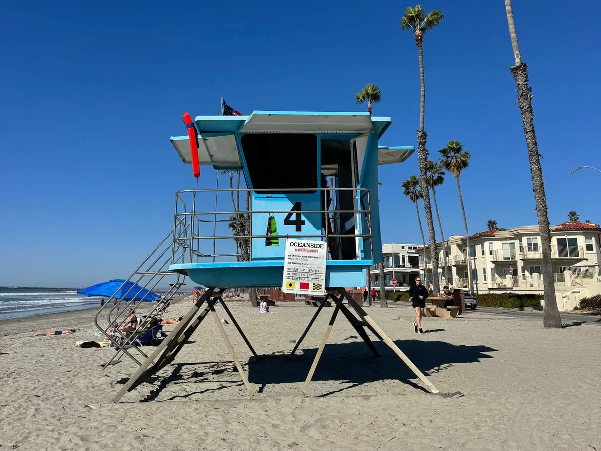 Lifeguard Tower 4 on the beach in Oceanside, CA, with palm trees and beachfront homes along The Strand
